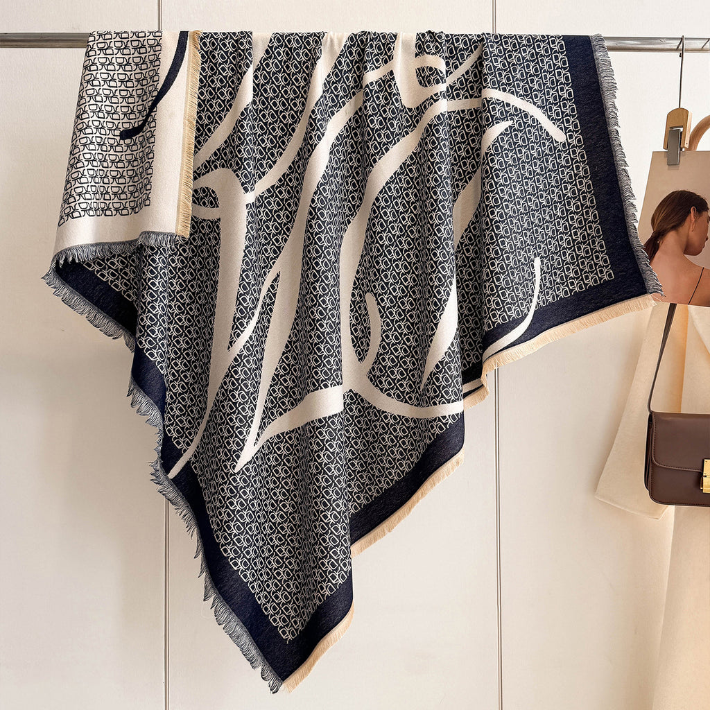 A patterned scarf with dark navy blue and cream abstract brushstrokes and a geometric lattice background, hanging from a clothing rack next to a mannequin wearing a brown shoulder bag.