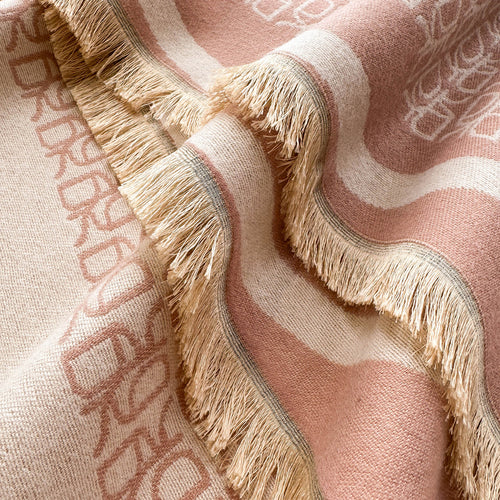 A close-up of a woven throw blanket with fringe, featuring a dusty pink and cream striped pattern with the brand name 'BURBERRY' woven into the fabric.