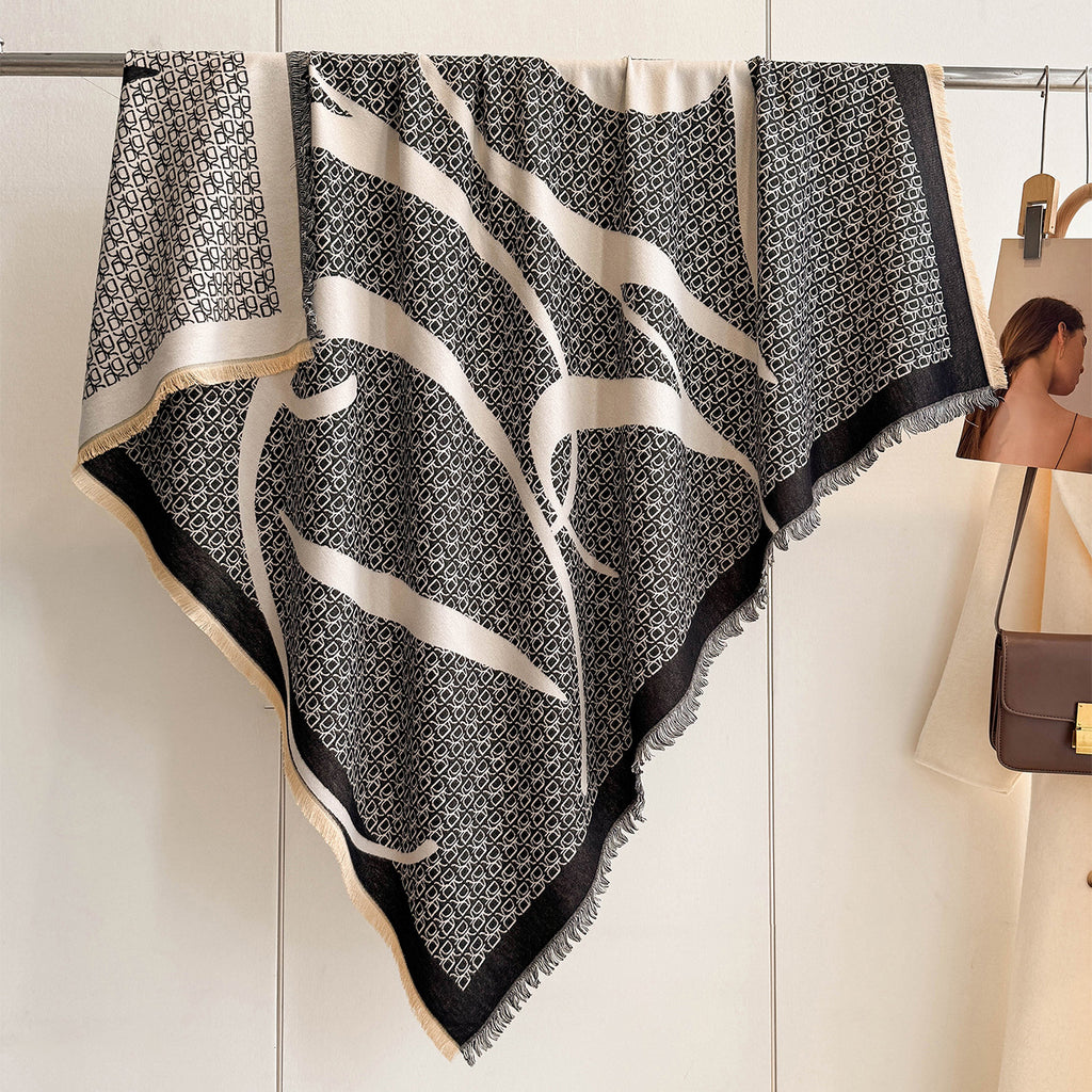 A black and beige patterned silk scarf with fringed edges draped over a clothing rack in a boutique setting.