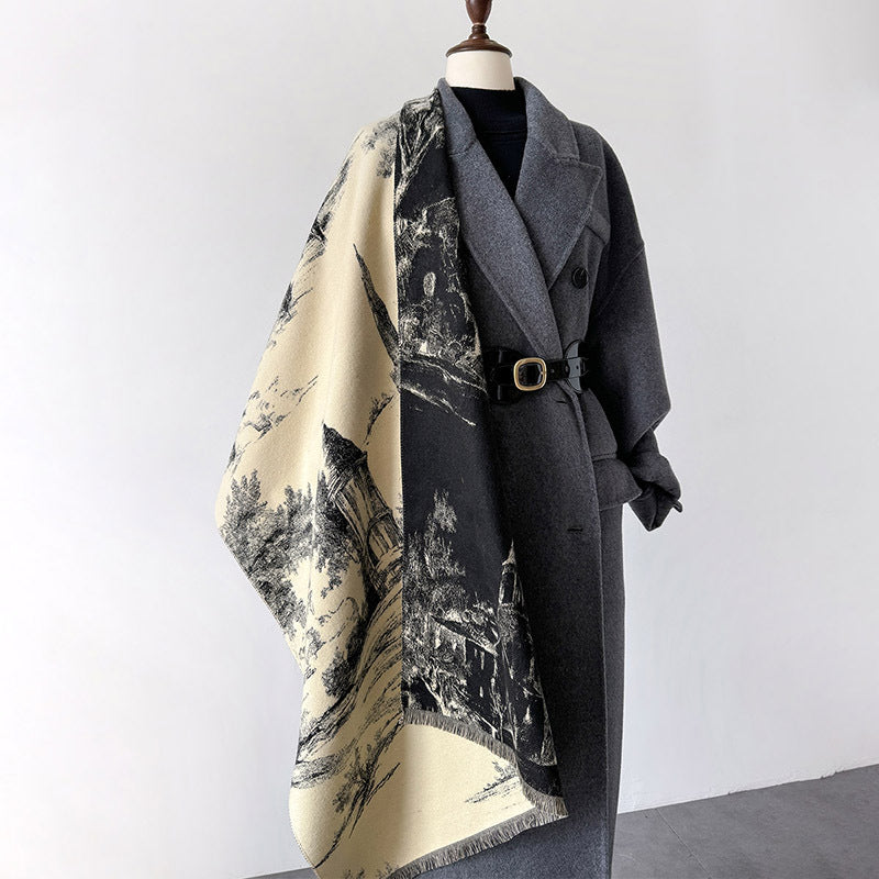 A long gray belted coat displayed on a mannequin torso, wrapped with a large cream and black scenic print scarf or shawl featuring landscape imagery.