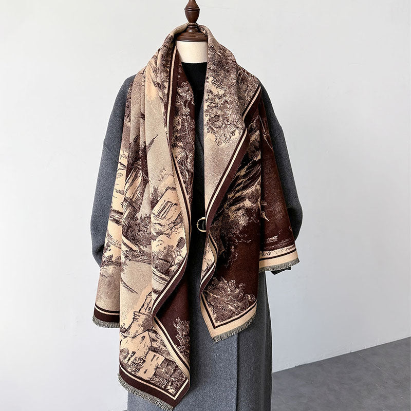 A large woven scarf with a scenic landscape print in beige, brown, and cream tones, draped over a gray coat on a mannequin against a plain light gray wall.