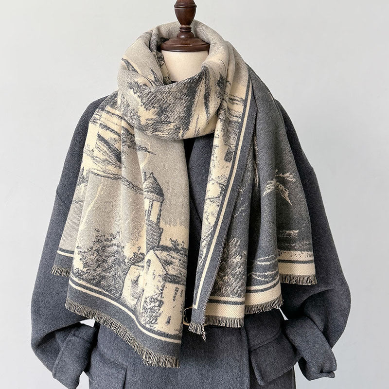 A large woven scarf with a beige and gray scenic landscape print, draped on a dark gray coat displayed on a mannequin against a light gray background.