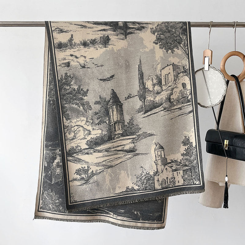 A folded scarf with a classic toile-style landscape print in beige and black hangs from a metal rod, styled with fashion accessories like a handbag, mirror, and pouch against a plain white wall.