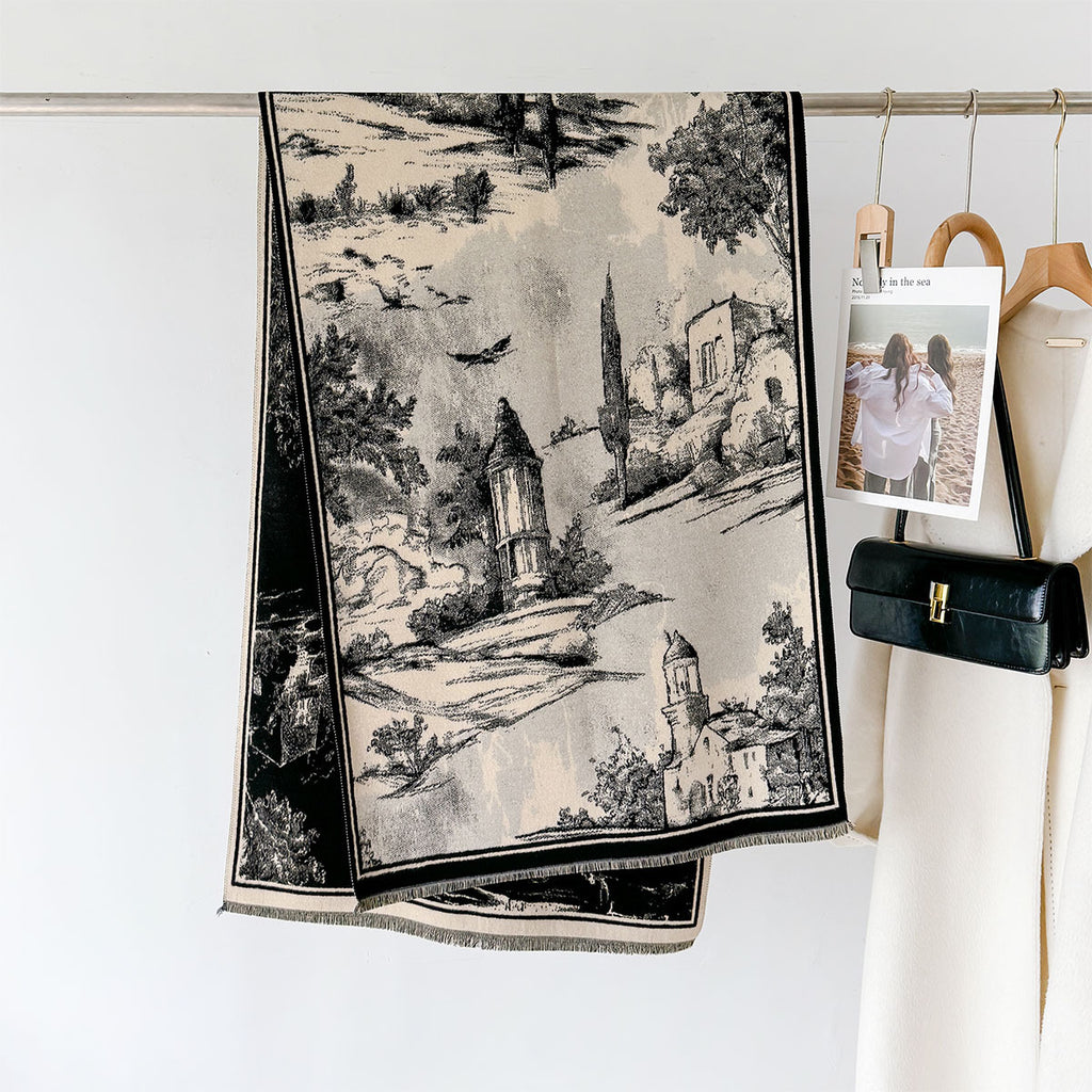 A black and beige woven scarf with a scenic landscape print hangs from a metal rod on a white wall, styled next to a cream-colored coat and a black handbag.