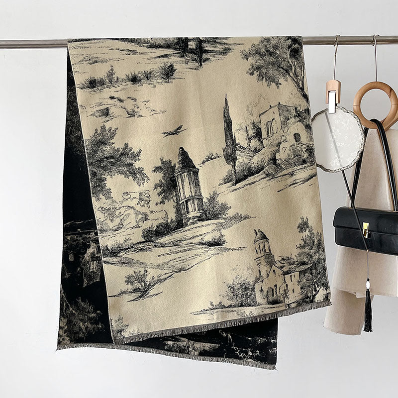 A woven throw blanket with a classic toile landscape print in beige and black hangs from a metal rod on a white wall, styled with a handbag and other accessories.