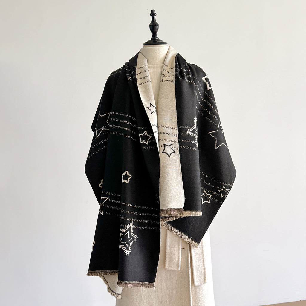 A black shawl with white embroidered star patterns and fringed edges, draped over a cream-colored coat on a mannequin against a plain light gray background.