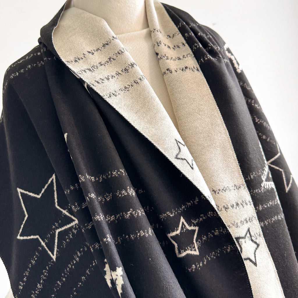 A black knit wrap or shawl with a cream-colored inner lining and embroidered star motifs, displayed on a mannequin torso against a plain white background.