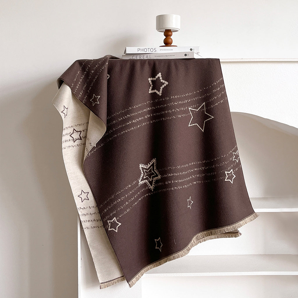 A dark brown throw blanket with white embroidered stars and stripes draped over a white shelf, showing a cream reverse side with text patterns.
