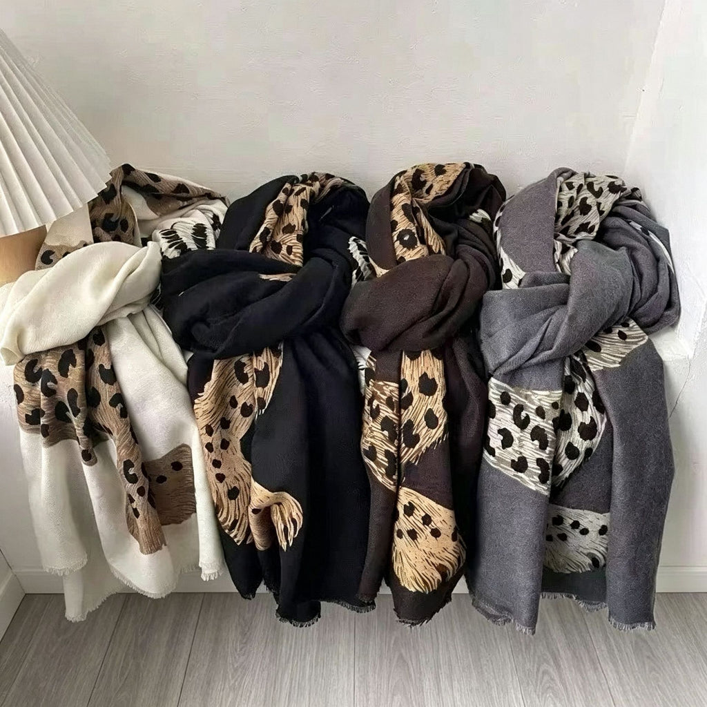 Four lightweight scarves with mixed animal print patterns are draped side-by-side on a light gray floor against a white wall.