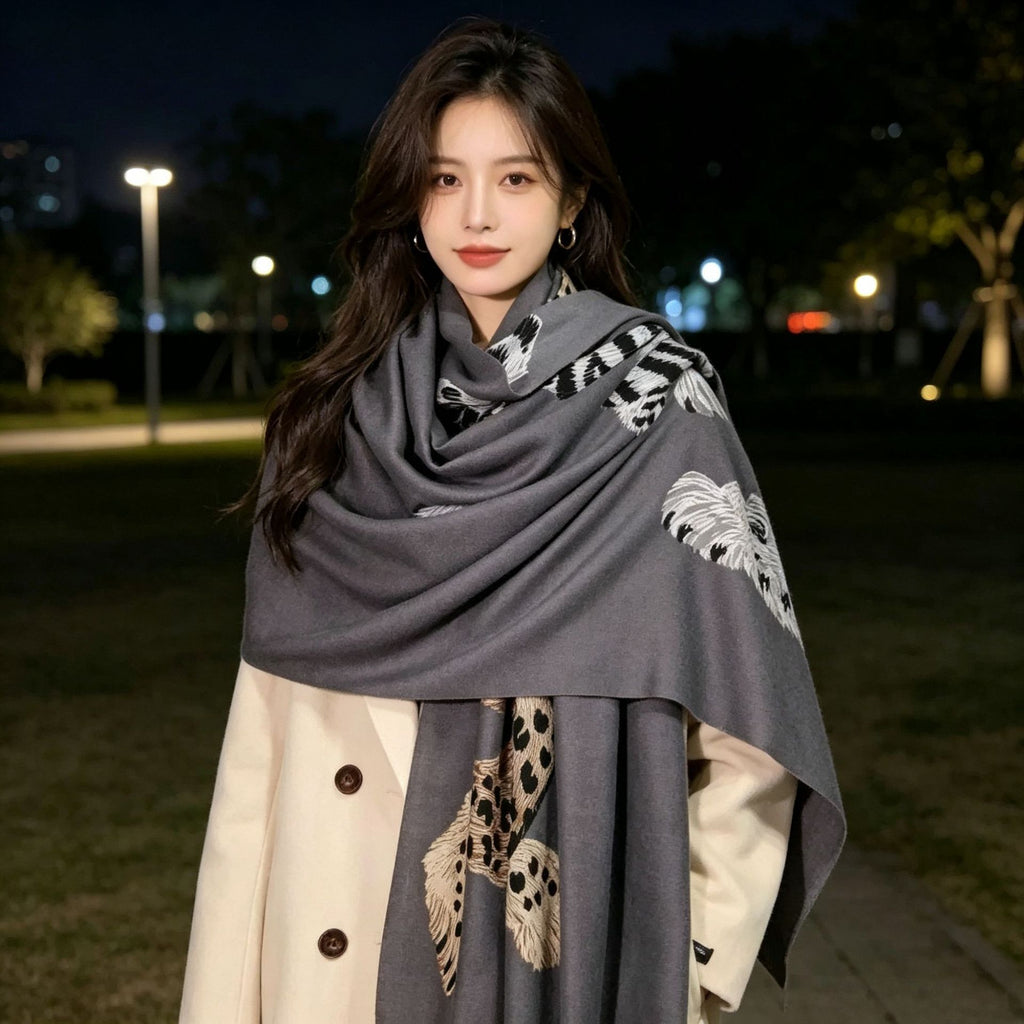 A woman wearing a dark gray shawl with white and beige animal print patterns, styled over a cream-colored coat at night in an outdoor park setting.